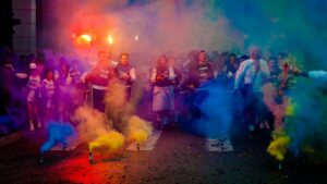 Front Page A lively group celebrating at night with color smoke bombs in a street festival.